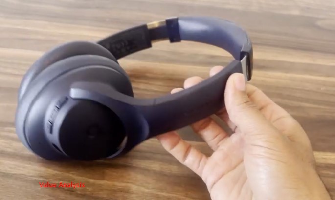 Hand holding Soundcore Q20i headphones over a wooden table