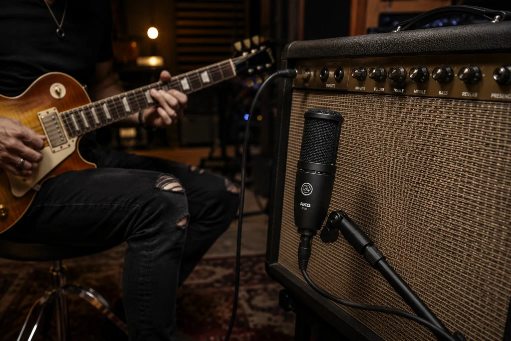 AKG P120 condenser microphone on a stand in front of a guitar amplifier while a guitarist plays an electric guitar